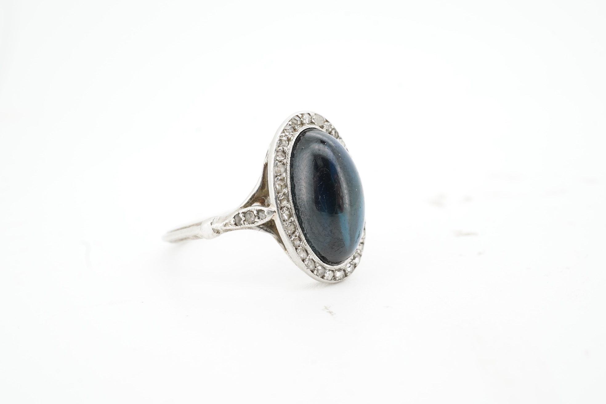 A sapphire and diamond ring, 1920s, set with a cabochon sapphire measuring approximately 2.4 x 6.8 x 4.7mm, within a border of rose-cut diamonds, mounted in platinum, size L1/2